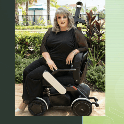 A woman sits in an accessible wheelchair in front of a palm tree.