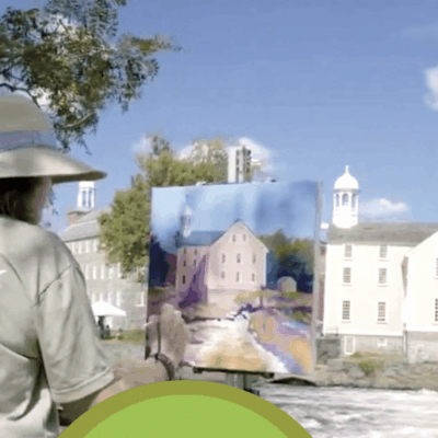 A woman in a hat is creating art in front of a river.