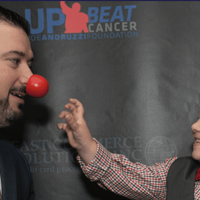 A man in a suit and tie alongside a little boy wearing a red nose, representing the Joe Andruzzi Foundation's philanthropic efforts.