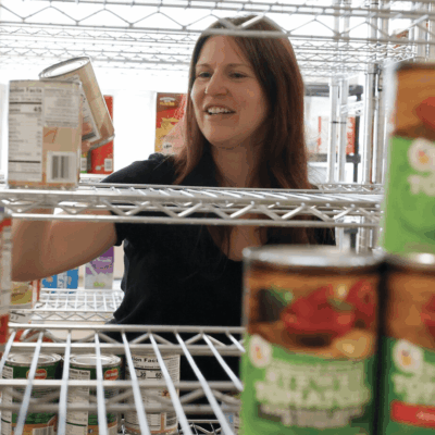 In a food pantry, a woman examines canned food options.