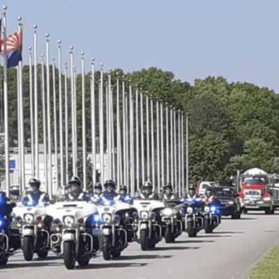 A group of police officers riding motorcycles down a street with flags, forming a motorcycle convoy.