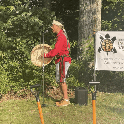 A man in a native outfit standing in front of a veterans sign.