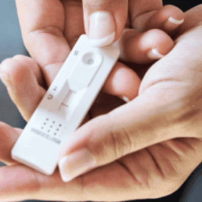 A woman's hand holding a digital thermometer for COVID tests.