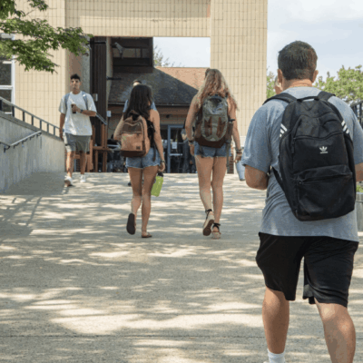 A group of URI students walking down a sidewalk with backpacks.