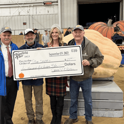 Three people holding a check in front of a giant pumpkin.