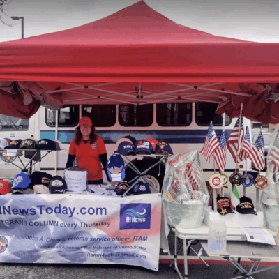 A woman stands at a table with veterans hats and flags.