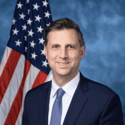 A man in a suit and tie standing in front of an american flag.