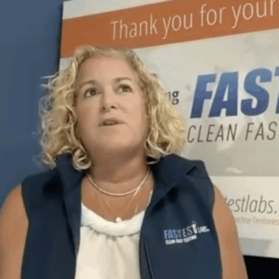 A woman is standing in front of a sign saying thank you for fast clean Fastest Labs.
