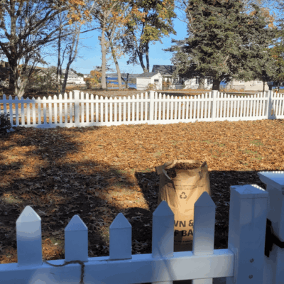 A white picket fence in a yard surrounded by leaves.