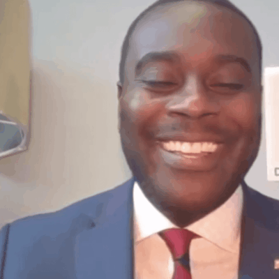 Gabe Amo, a man in a suit and tie, is smiling.