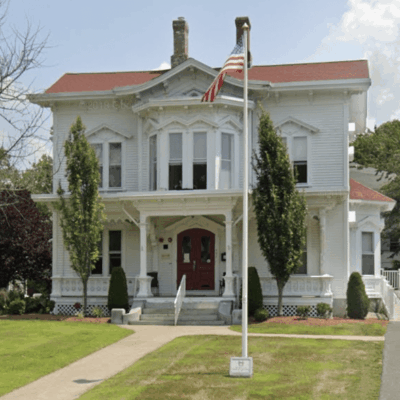 A white victorian house with a flag on the front porch, providing housing for veterans.
