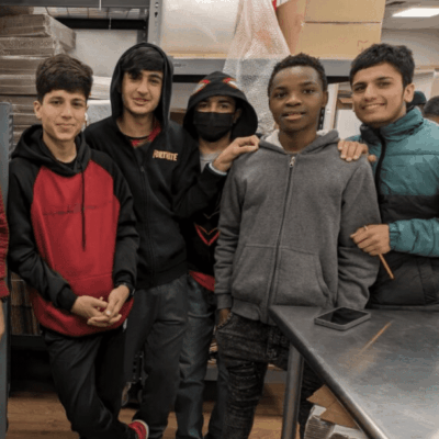 A group of young Afghan refugees posing for a photo in a kitchen.