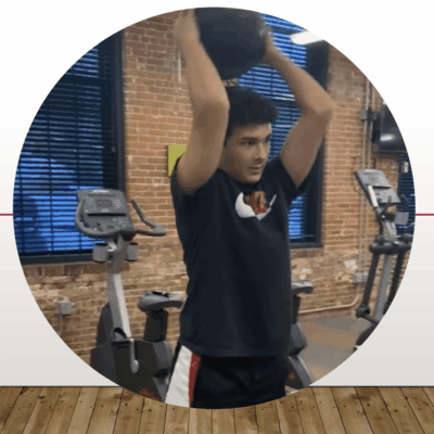 A man performing an exercise of lifting a ball in a gym.