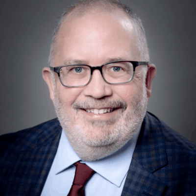 A man wearing glasses and a suit smiles for the camera.