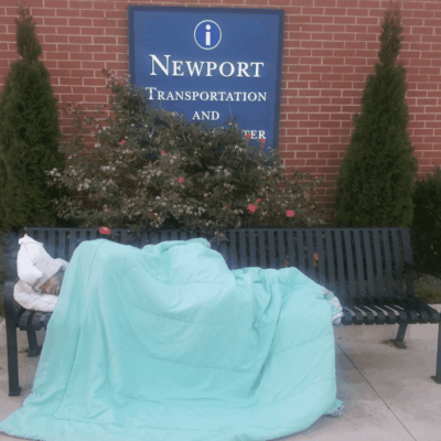 A homeless person sleeping on a bench in front of a building in RI.