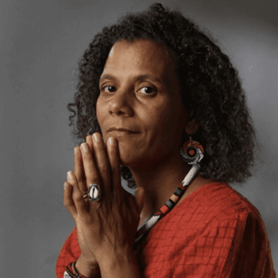 A woman with curly hair is captivated by black storytelling as she poses with her hands clasped.