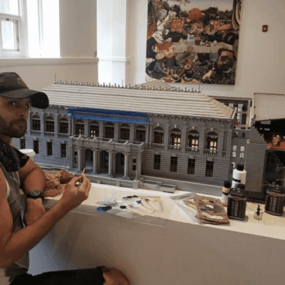 A man sitting in front of a legos model of a building.