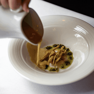 A person pouring a sauce into a white bowl.