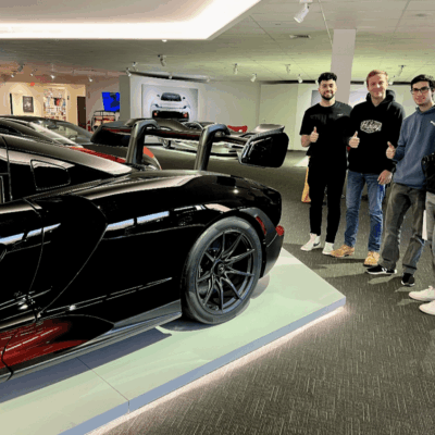 A group of men standing next to a black sports car in a car museum.