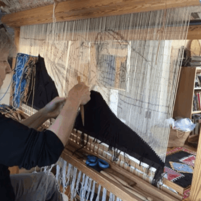 A woman is creating art on a wooden loom.