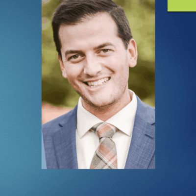 A man in a suit and tie smiles at the SBA Awards in front of a blue background.
