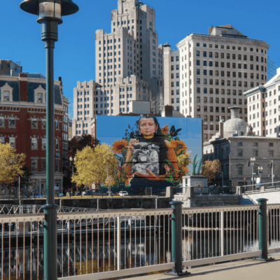 Mural of woman, city buildings backdrop
