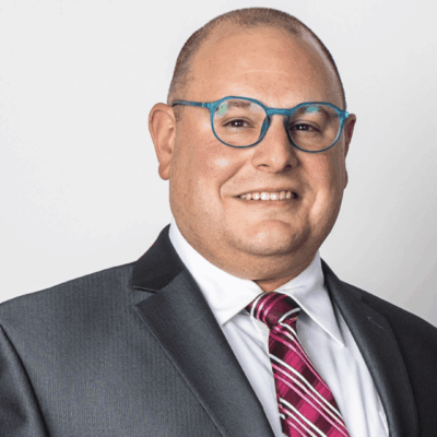 Here's an alt tag for the image: Man in suit and blue glasses.