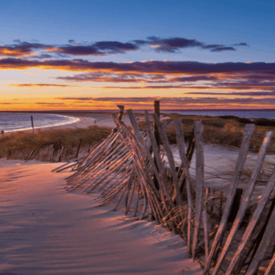 Sunset beach scene with wooden fence.