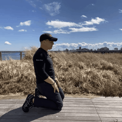 Man kneeling outdoors by the ocean.