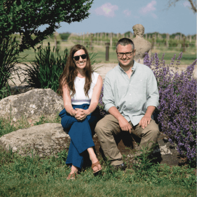 Couple sitting on rocks by vineyard.
