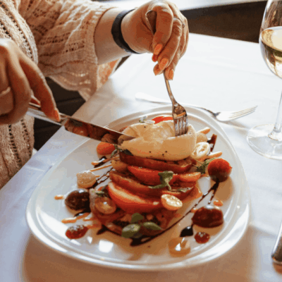 Person cutting burrata salad with knife and fork.