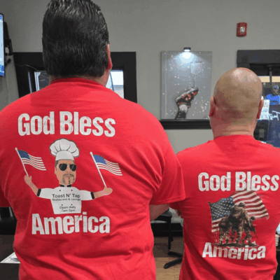 Two men wearing red shirts with the words " god bless america " on them.
