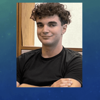 A man with curly hair and black shirt smiling.