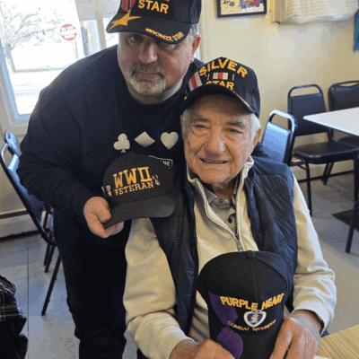 Two men are holding hats and posing for a picture.