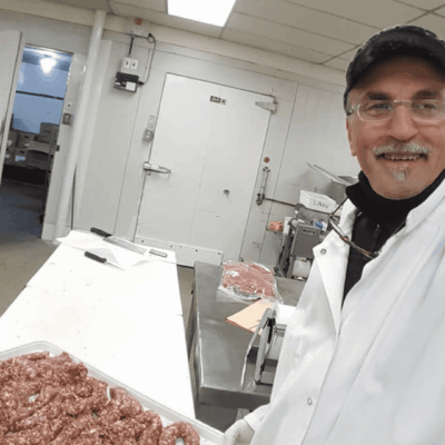 A man in white lab coat holding a box of meat.