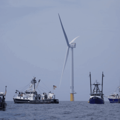 A group of boats in the ocean with a wind turbine.