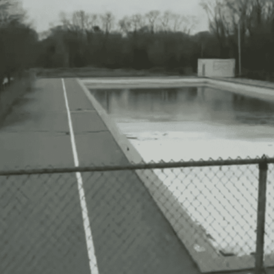 Empty outdoor swimming pool with surrounding fence.