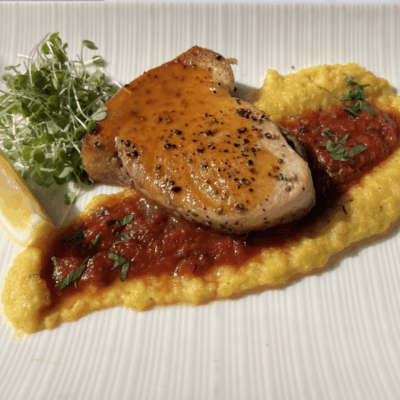 Grilled chicken with sauce, microgreens, and polenta.