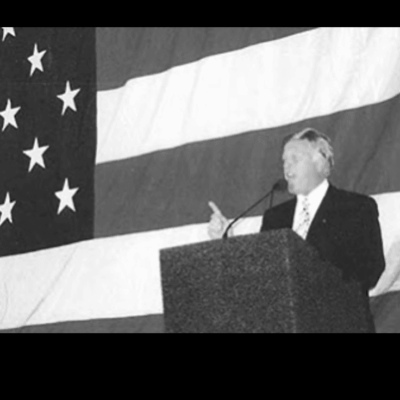 A man in suit and tie speaking at podium.