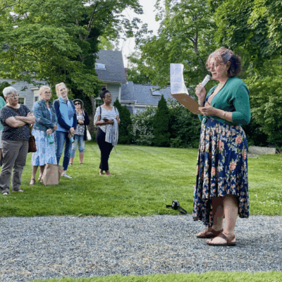 A woman standing in the grass holding papers.