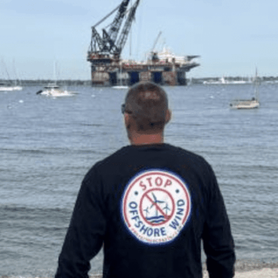 A man standing on the beach looking at an oil rig.