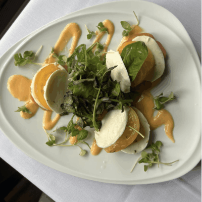 A fresh salad with greens, orange slices, and mozzarella cheese on a white plate.