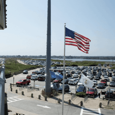 An American flag waving over a busy parking lot near a waterway.