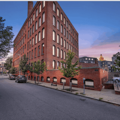 Brick building on a street corner during sunset with trees and parked cars.