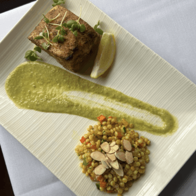 Elegant plated dish with meat, green sauce, and a grain salad.