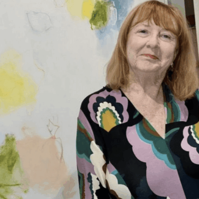 A woman with red hair stands in front of a colorful abstract painting.