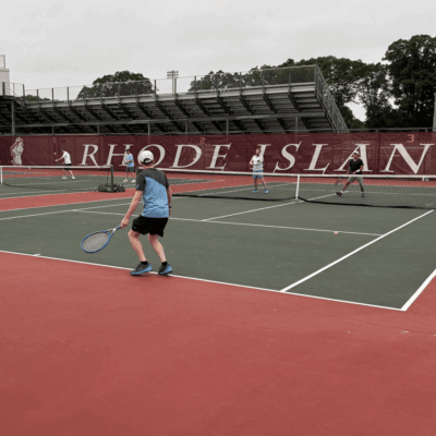 Players compete on a Rhode Island tennis court under cloudy skies.