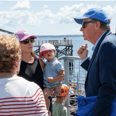 People conversing near a waterfront with a bridge in the background.