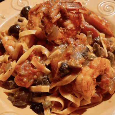 A plate of pasta with shrimp, olives, and tomato sauce.