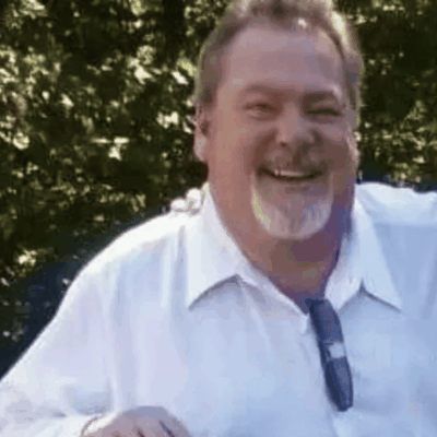 A cheerful man in a white shirt smiling outdoors.